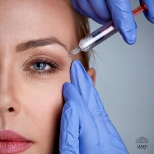 Rosto feminino em primeiro plano, recebendo aplicação de produto para preenchimento facial na região das pálpebras.