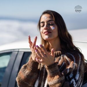 Mulher jovem em primeiro plano, passando protetor solar nas mãos e no rosto