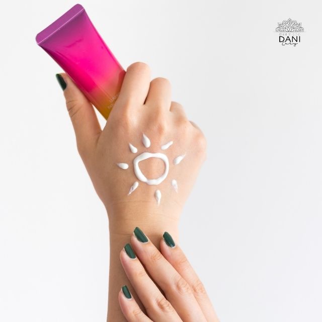 Mão feminina em primeiro plano, com um desenho de sol na mão feita com protetor solar, segurando uma embalagem de protetor solar